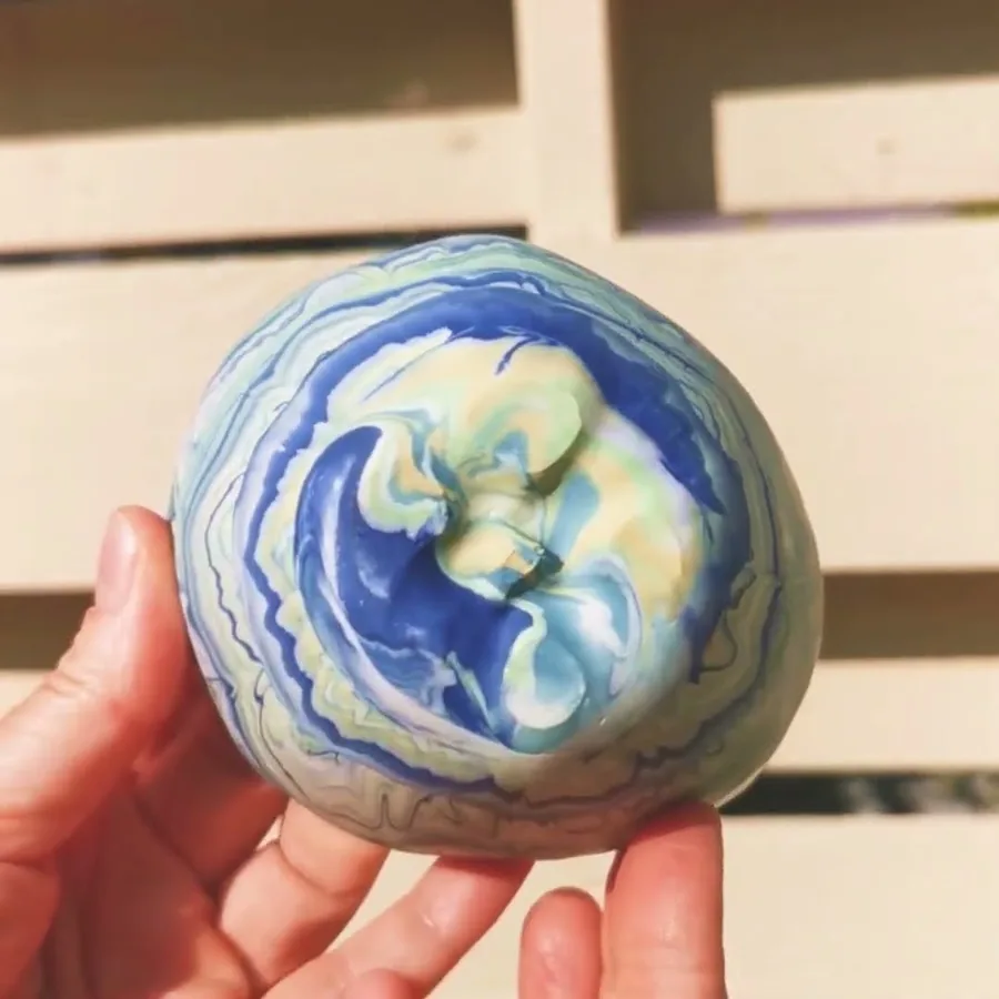Video of a hand turning a blue, green and cream marbled ceramic bowl in the sun