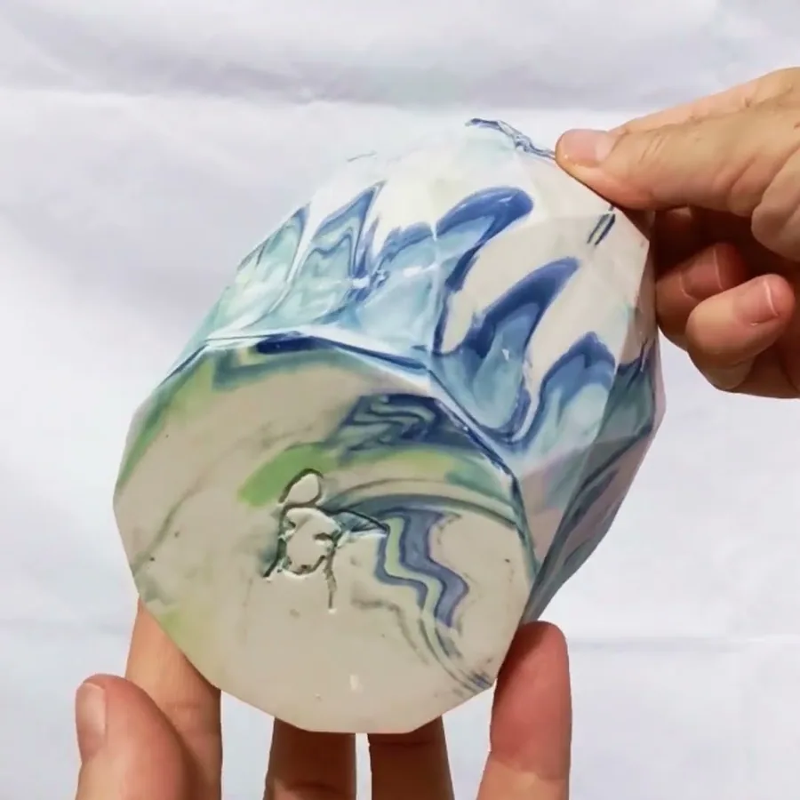 Video of a hand turning a blue and green marbled ceramic vase