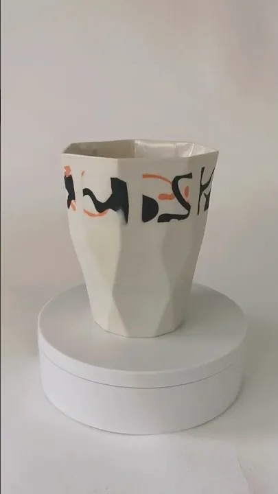 Video of a white ceramic vase with black and orange marks turning on a plinth